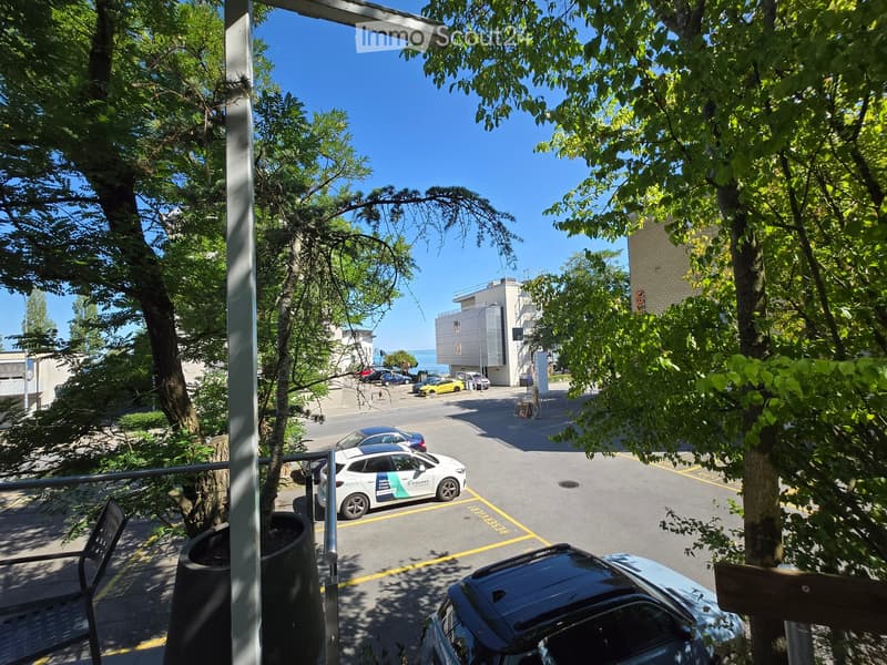 Balcony overlooking a street with parked cars, trees, and a view of the ocean in the distance.