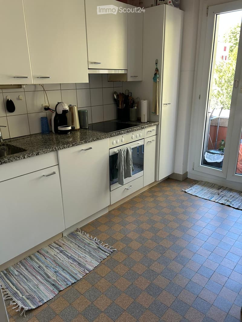 A modern kitchen with white cabinets, a granite countertop, and a tiled floor. Features include a refrigerator, oven, coffee maker, sink, and various kitchen utensils.
