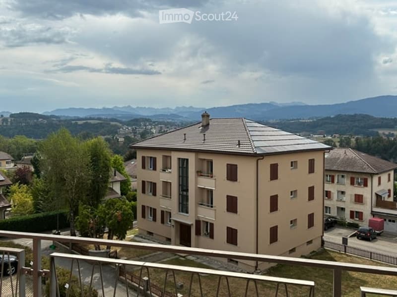 Multi-story residential building with balconies and large windows, overlooking a scenic valley and distant mountains.