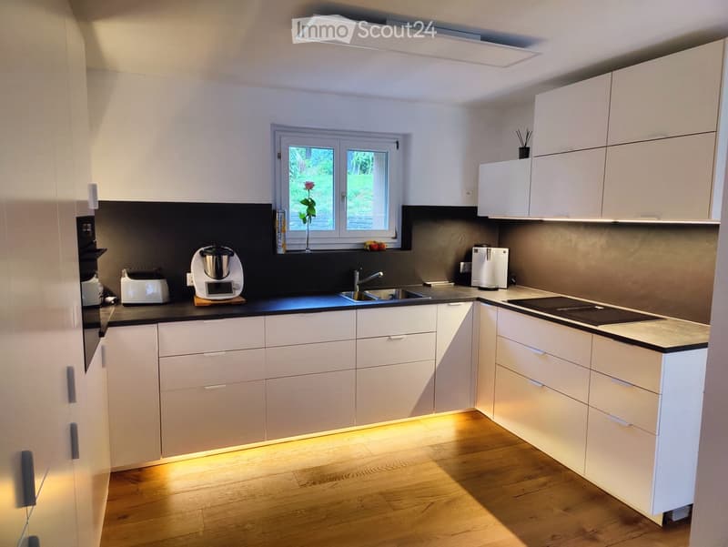 modern kitchen, white cabinets, black countertops, wooden floor, kitchen island, gas stove, sink, coffee maker, refrigerator, flower vase
