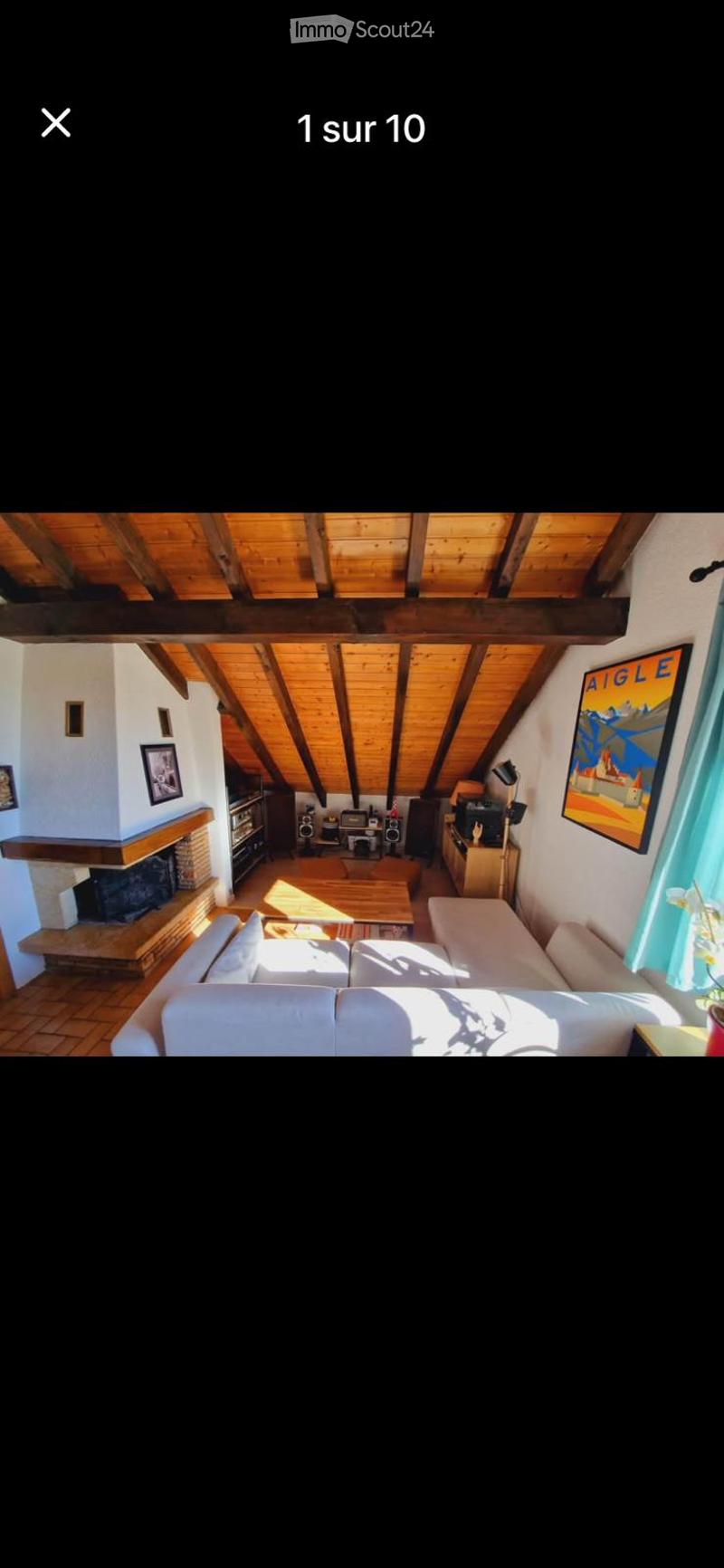 Living room with exposed wooden beams, fireplace, sofa, coffee table, and wooden floor.