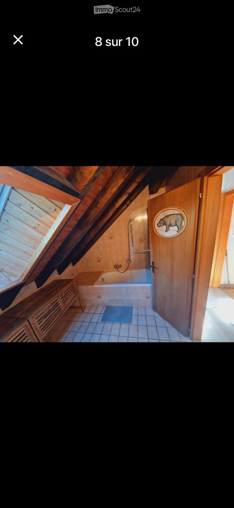 Cozy attic bathroom with wooden beams, a bathtub, a wooden cabinet, and a bathroom door with a decorative round emblem.