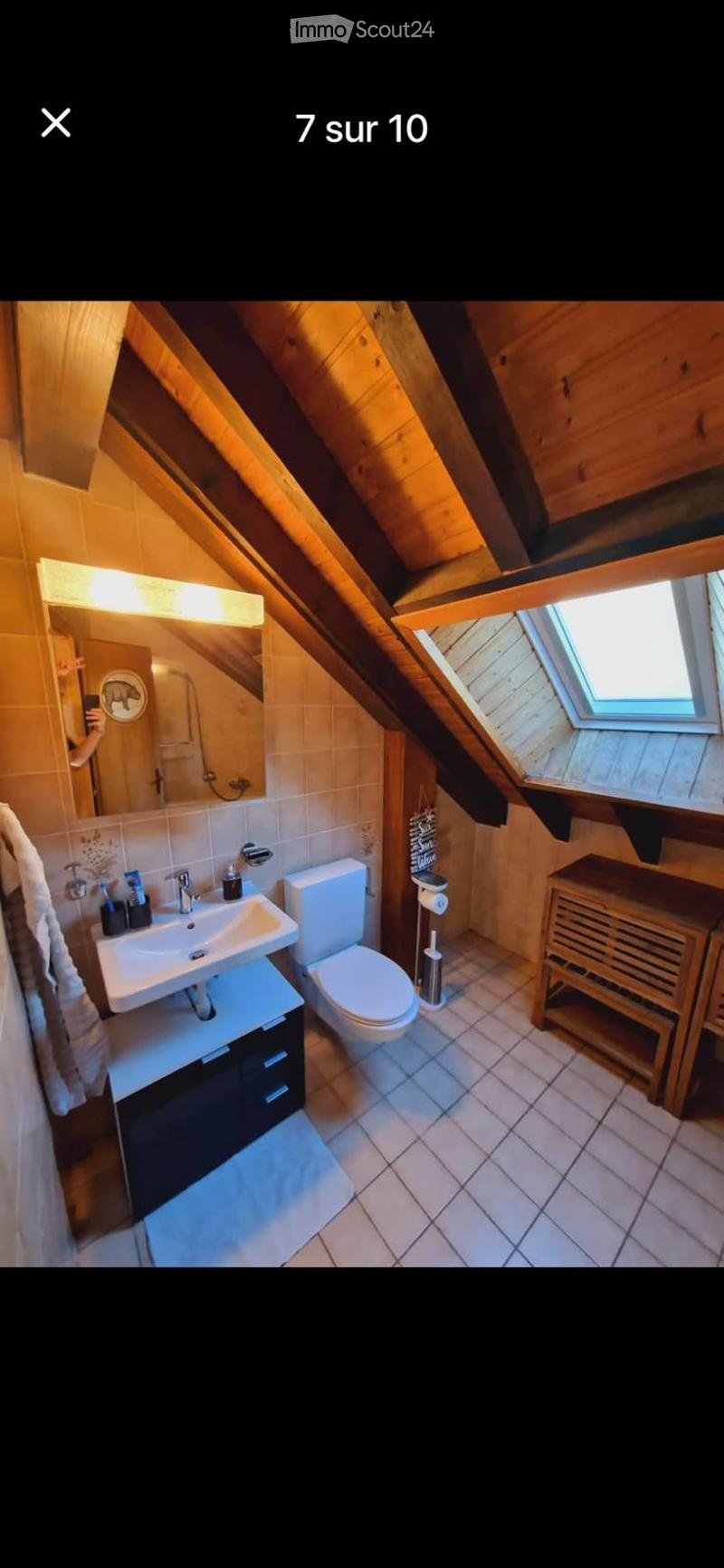 Cozy attic bathroom with wooden beams, a sink, toilet, mirror, and a skylight window providing natural light.