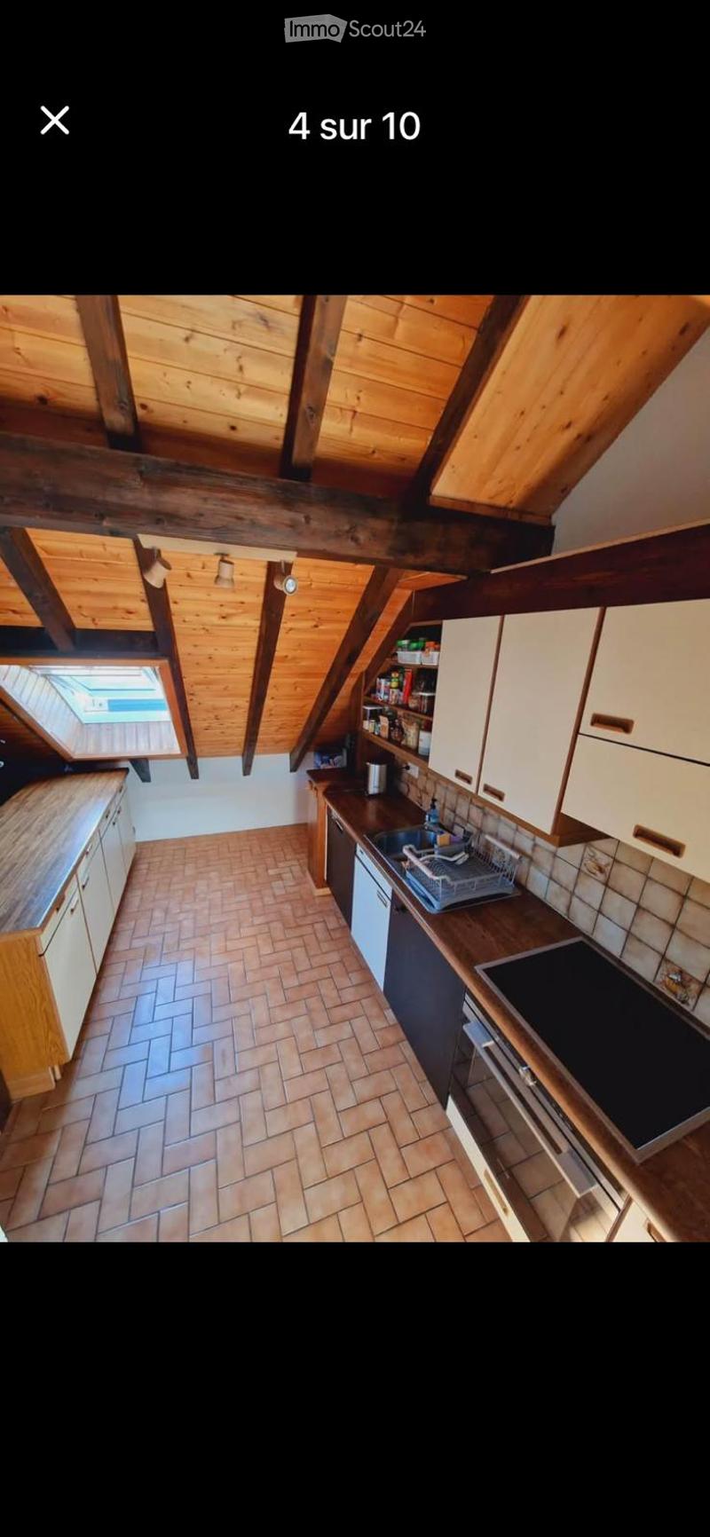 The kitchen features exposed wooden beams and a wooden ceiling, with white cabinets, a wooden countertop, and a tiled floor. Appliances include a sink, stove, oven, and refrigerator. A dish rack is visible on the counter.
