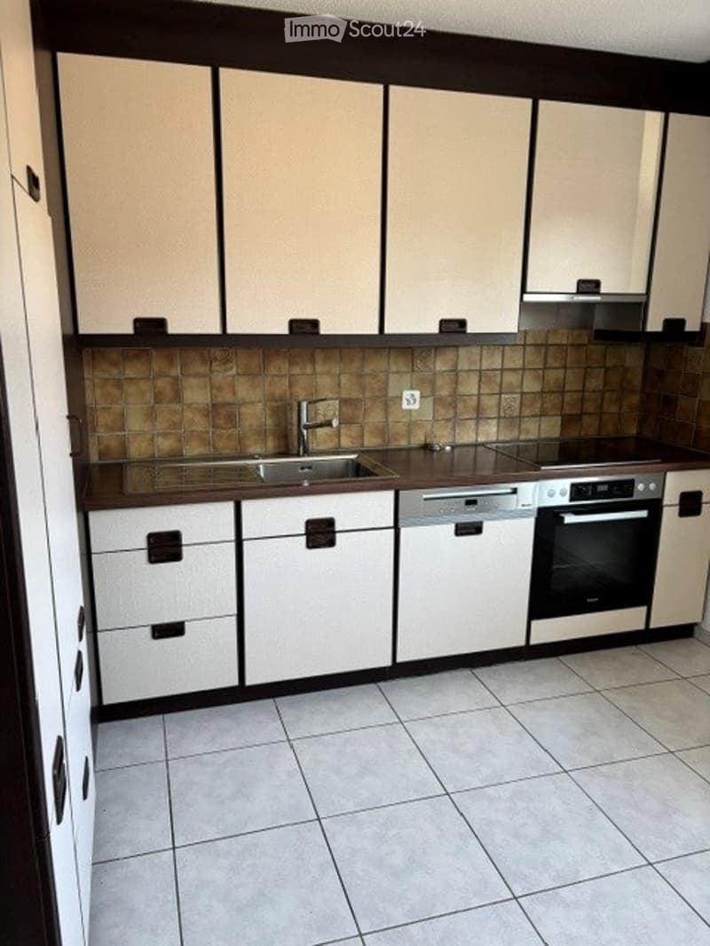 Modern kitchen with white cabinets, tiled backsplash, stainless steel sink, dishwasher, and oven.