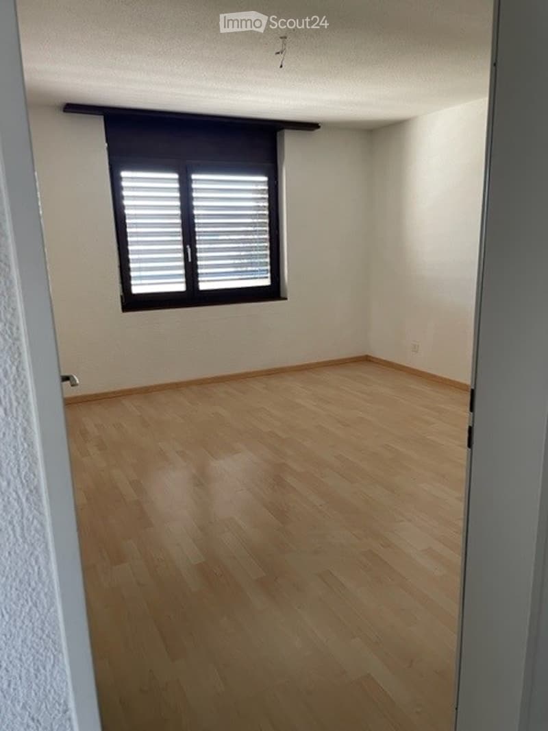 Empty room with wooden flooring, white walls, and a window with blinds.