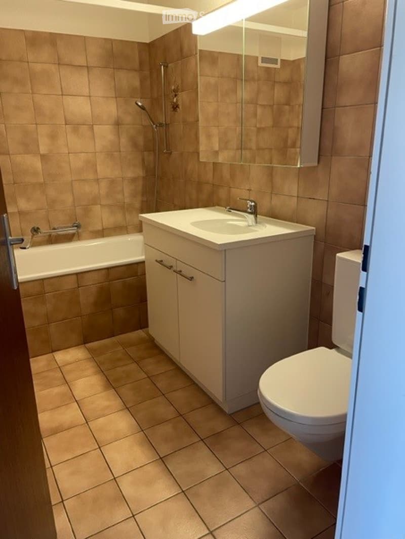 Modern bathroom with beige tiles, a white sink with a cabinet, a toilet, a bathtub, and a shower area with a glass enclosure.