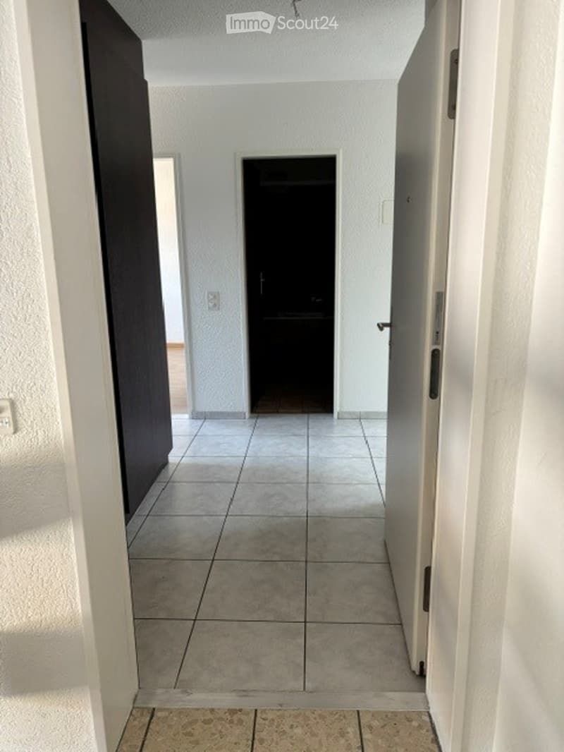 Empty hallway with tiled floor, white walls, and several doors leading to other rooms.