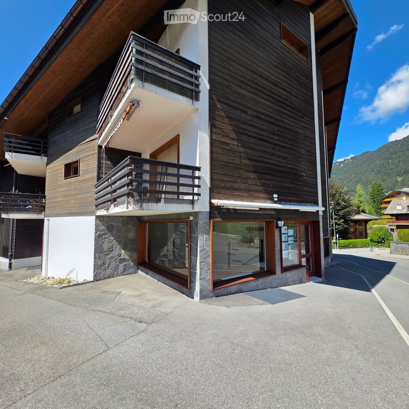 Modern two-story building with wooden and stone facade, multiple balconies, large windows, and a clear view of surrounding mountains.