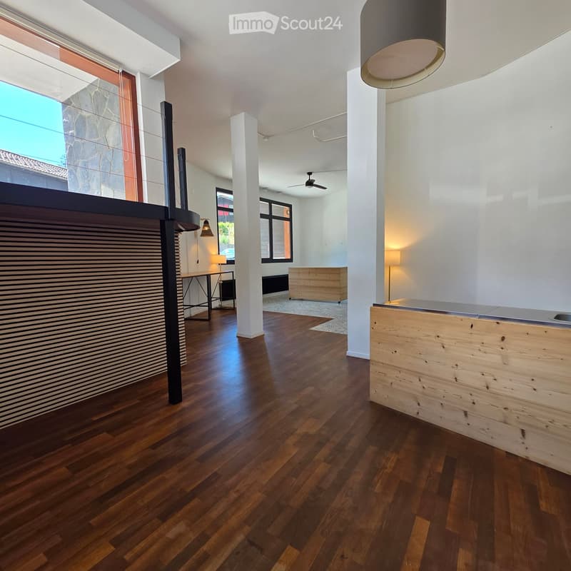 Modern hallway with polished wooden flooring, white walls, and contemporary lighting fixtures. Features include a sleek black reception desk, a wooden cabinet, and a small table with chairs in the background.
