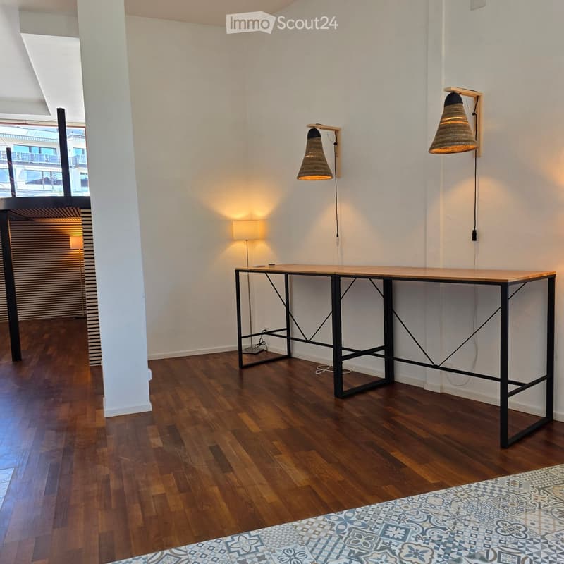 Minimalist room with wooden floor, white walls, a long black-framed table, floor lamp, and two wall-mounted lamps with woven shades.