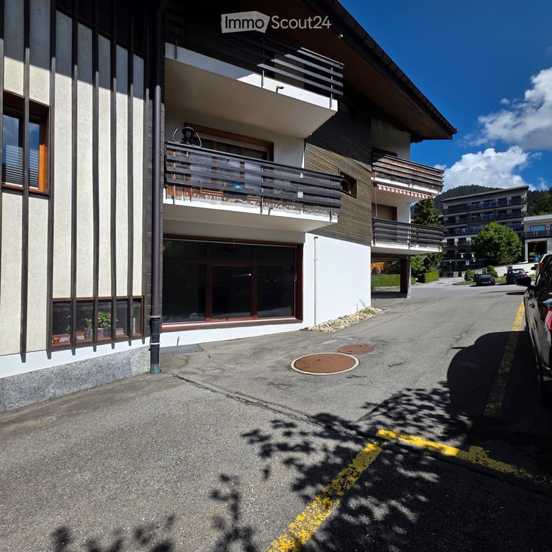 Modern multi-story building with balconies, large windows, and a paved driveway.