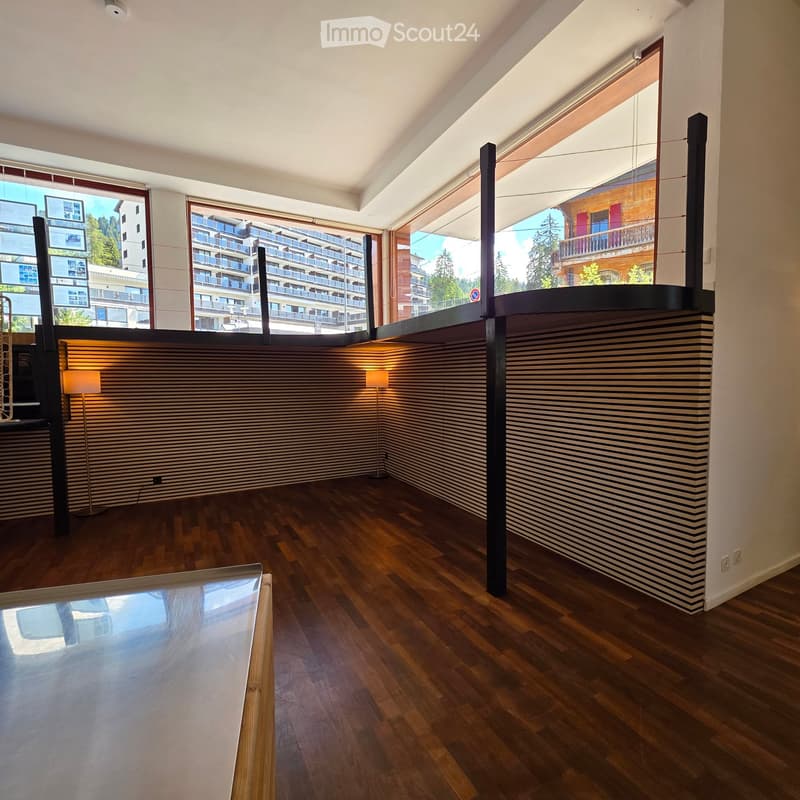 Empty room with wooden flooring, large windows, and modern decor including a glass table and striped wall paneling.