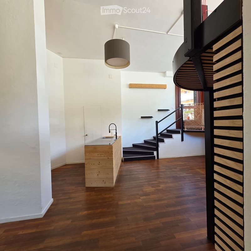 Modern hallway with wooden flooring, white walls, a staircase with a black railing, a pendant light fixture, and a small wooden counter with a sink.