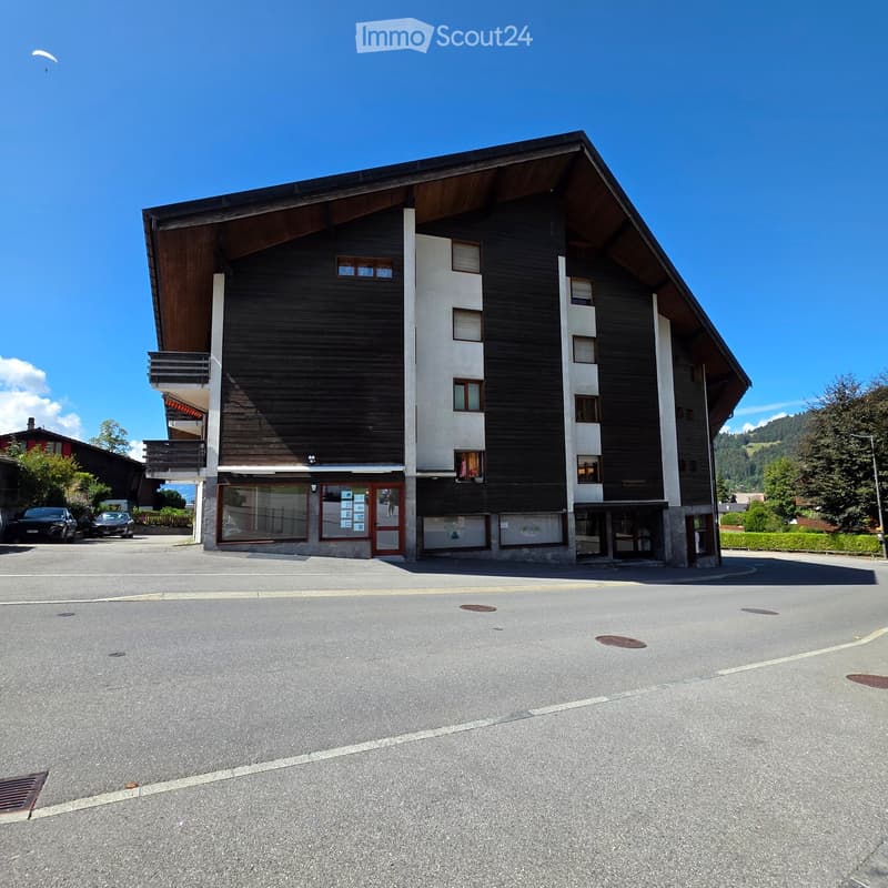 Modern multi-story building with wooden and white facades, balconies, and a parking area in front.