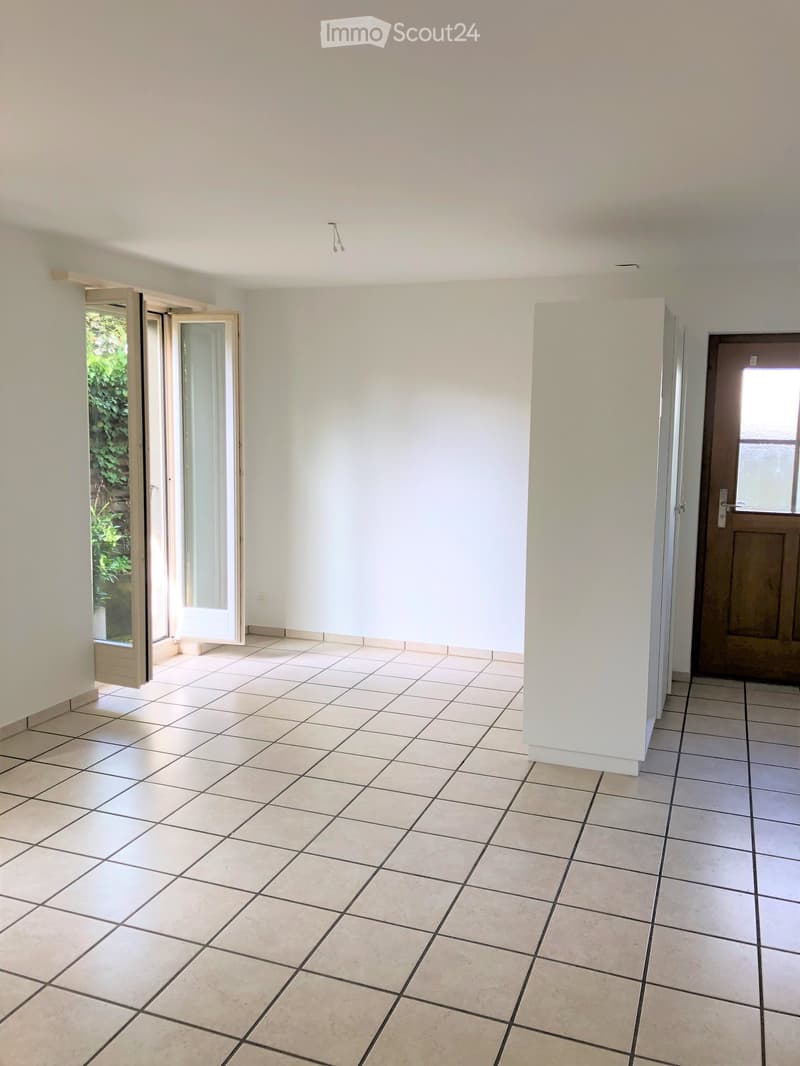 Empty room with tiled floor, white walls, and an open sliding door leading to a green outdoor area.