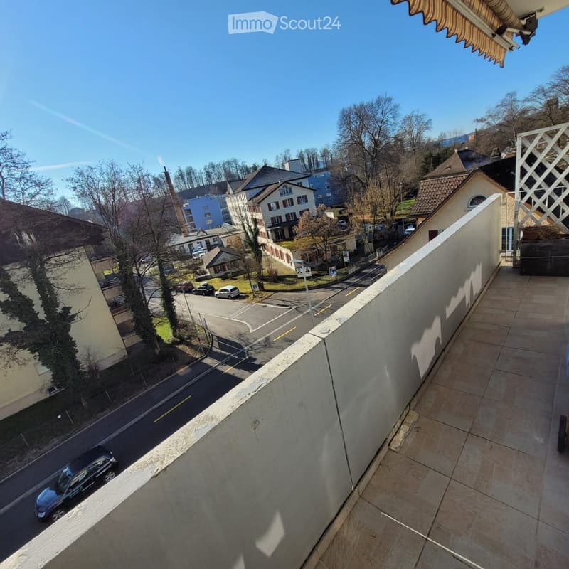 Balcony overlooking a street with parked cars, buildings, and trees in the background.