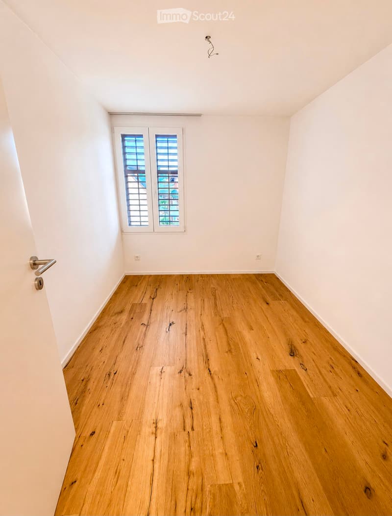 Empty room with light wooden flooring, white walls, and a window with blinds. No furniture or equipment is present.