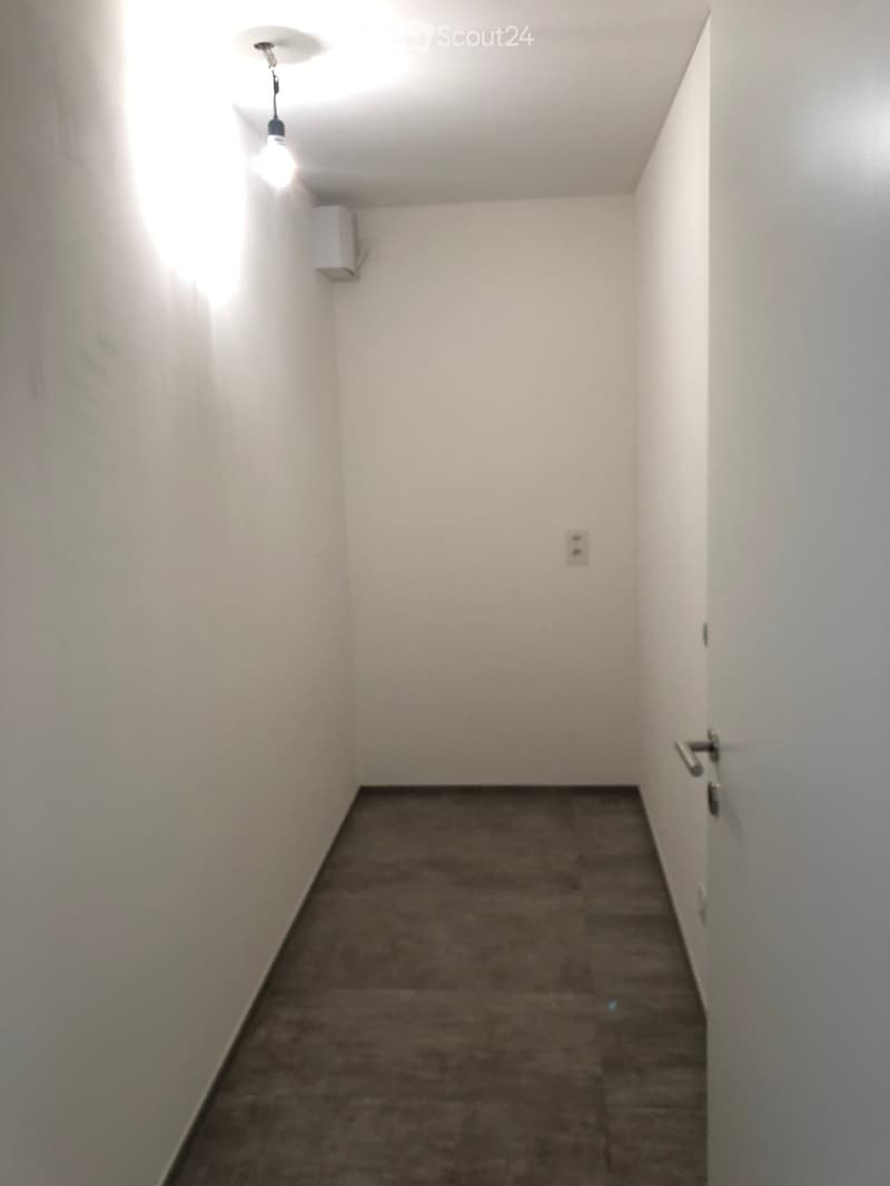 Empty hallway with white walls, gray tiled floor, and a single light fixture on the ceiling.