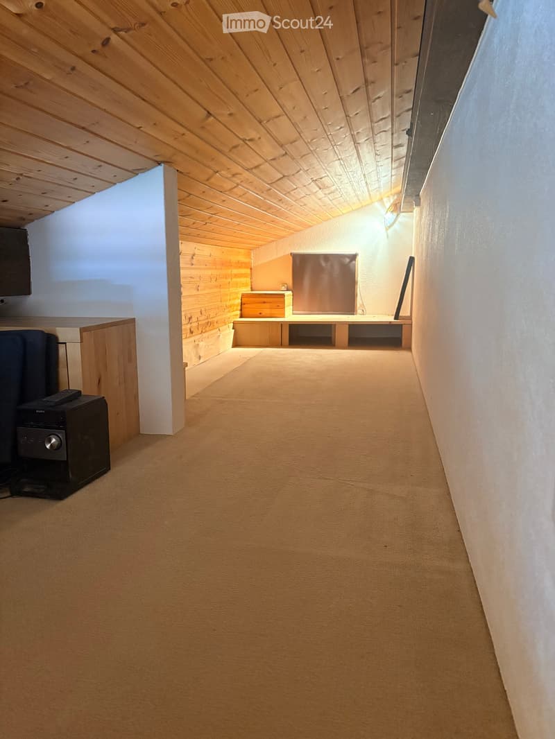 Carpeted hallway with wooden ceiling and walls, featuring a small seating area with bench and storage unit at the end.