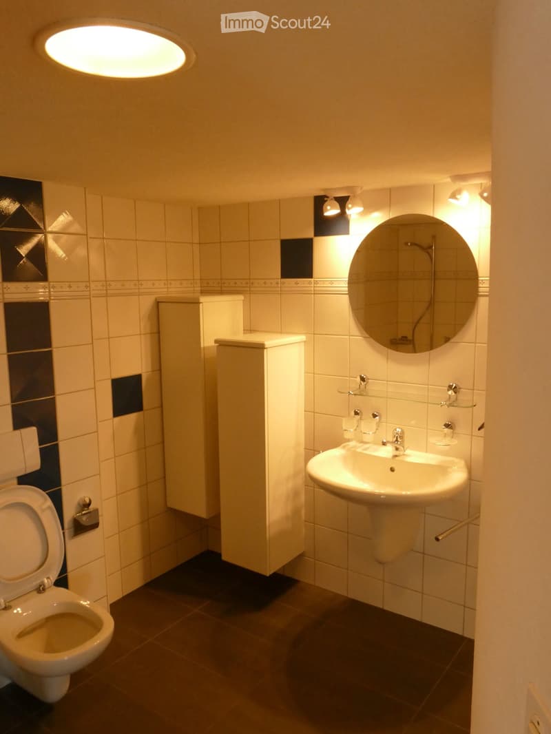 Modern bathroom with white tiles, a toilet, a sink with a mirror, and a cabinet. The walls feature a decorative black and white tile pattern, and the lighting is warm and ambient.