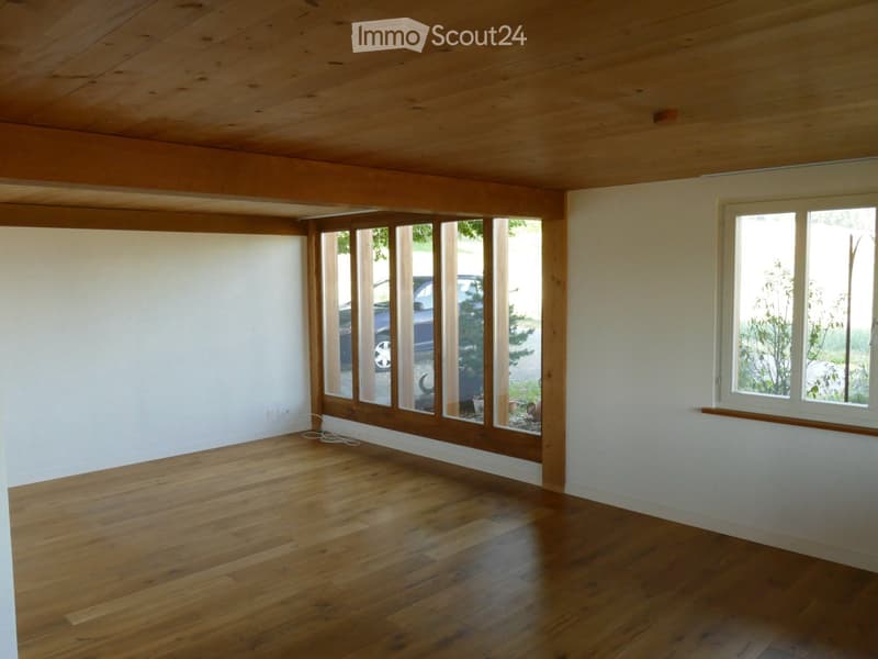 Empty room with wooden flooring, white walls, large windows, and a sliding glass door leading outside.