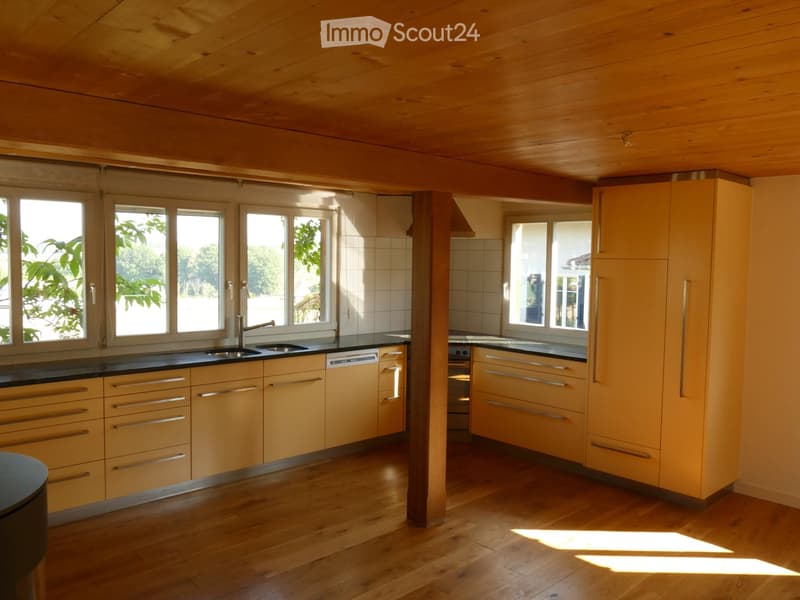 Bright kitchen with wooden cabinets, stainless steel sink, and modern appliances, featuring large windows and wooden flooring.