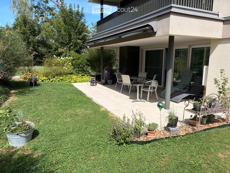 Well-maintained garden with a lawn, potted plants, and a patio area with outdoor furniture including chairs, a table, and lounge chairs.