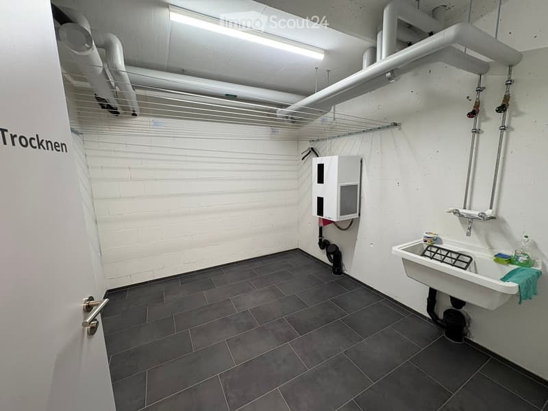 Modern bathroom with dark tiled floor, white brick walls, a white sink with a faucet, a water heater unit, and a drying rack.