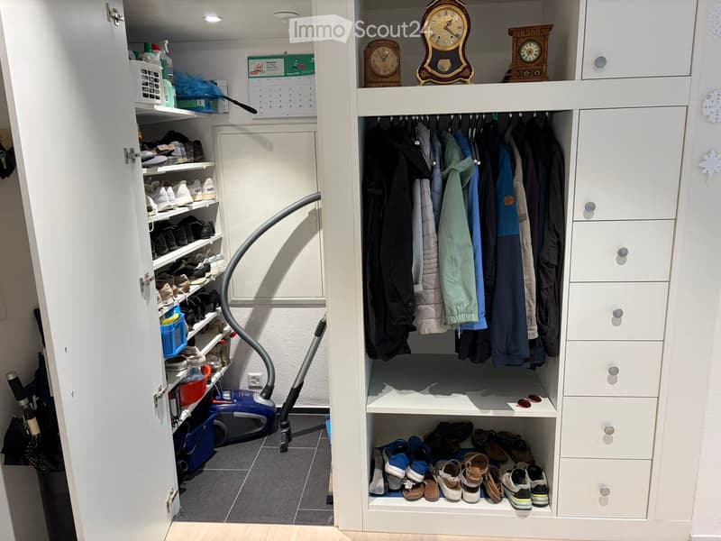 A well-organized walk-in closet with white built-in wardrobes, multiple shelves filled with shoes, hanging clothes, and decorative clocks on top.