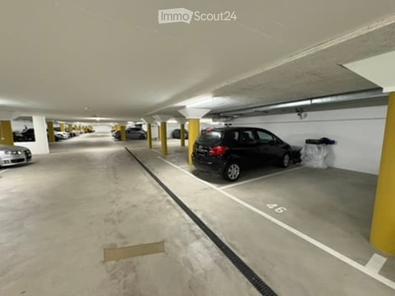 Underground parking area with several parked cars, yellow support pillars, and marked parking spaces.