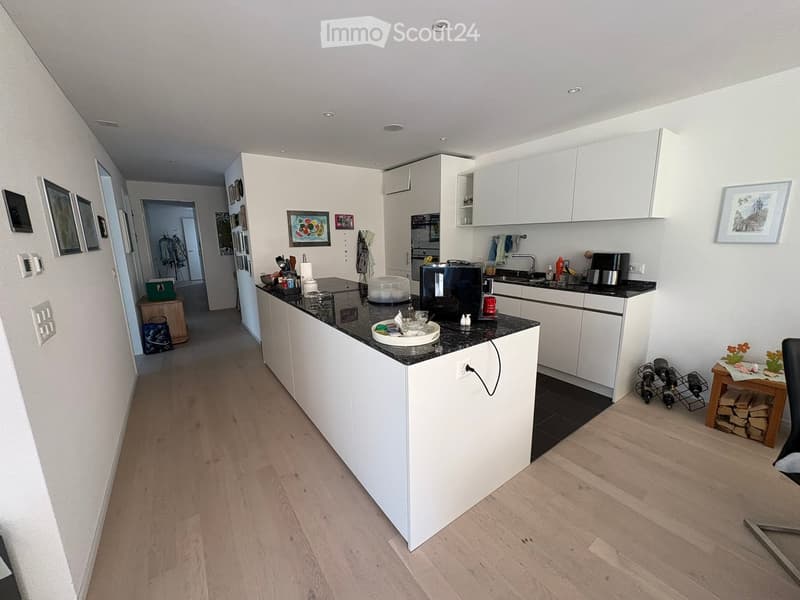 Modern kitchen with white cabinets, black countertop, and wooden flooring. Includes a sink, coffee maker, oven, fridge, wine rack, and framed pictures on the walls.