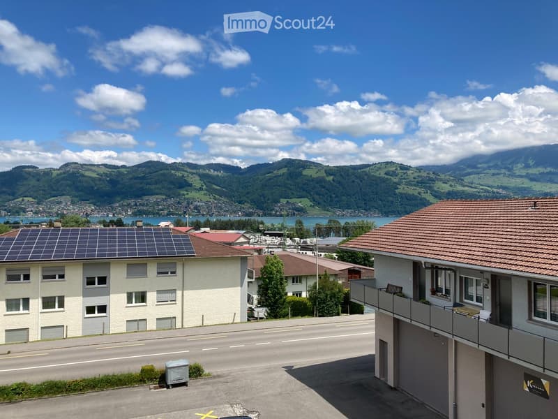 Residential buildings with solar panels on the roof, overlooking a scenic valley and lake with distant mountains.