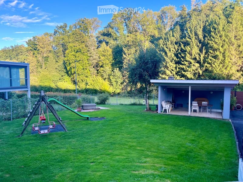 Well-maintained garden with a swing set, slide, and a covered patio area with a table and chairs.