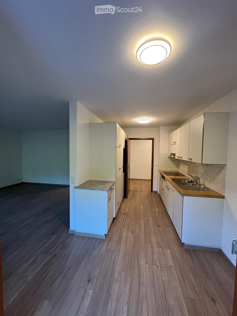 Modern kitchen with white cabinets, wooden countertops, and a sink area. The floor is made of light wooden planks, and the walls are painted in a neutral tone.