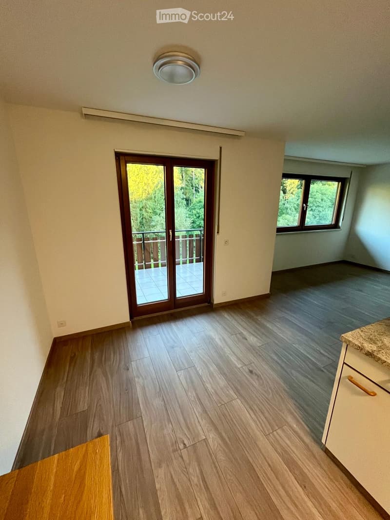Empty room with wooden flooring, a sliding glass door leading to a balcony, and a small window on the adjacent wall.