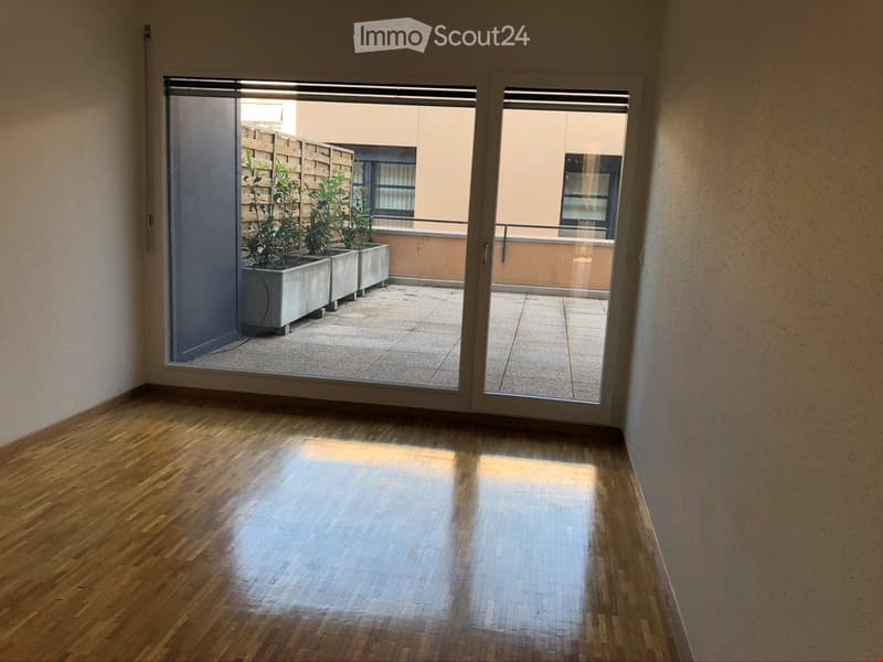 Empty room with wooden flooring and large sliding glass doors opening to a balcony area with potted plants.
