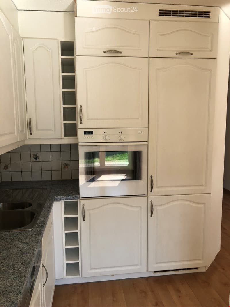 A modern kitchen with white cabinets, a built-in refrigerator, an oven, and a sink. The cabinets have glass-paneled doors and decorative handles.