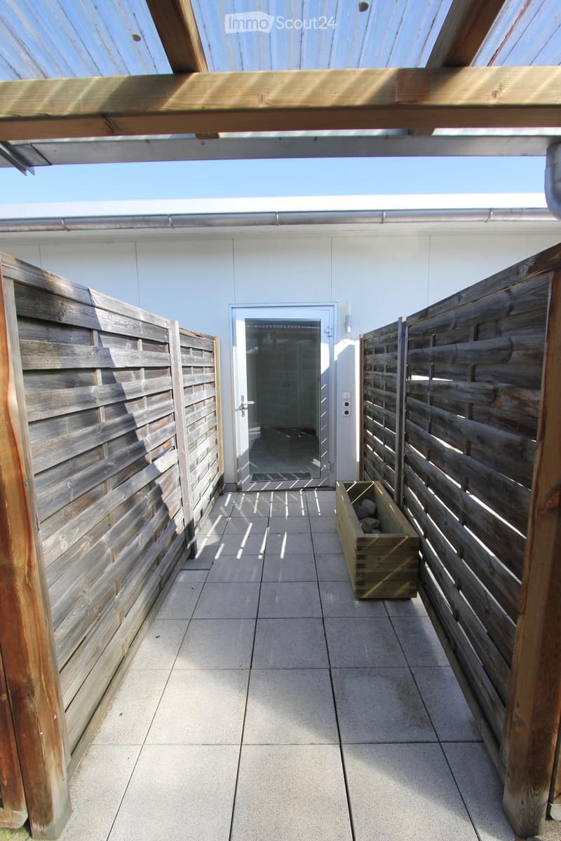 Wooden fence-lined balcony with tiled floor, glass door leading inside, and a small wooden planter box.