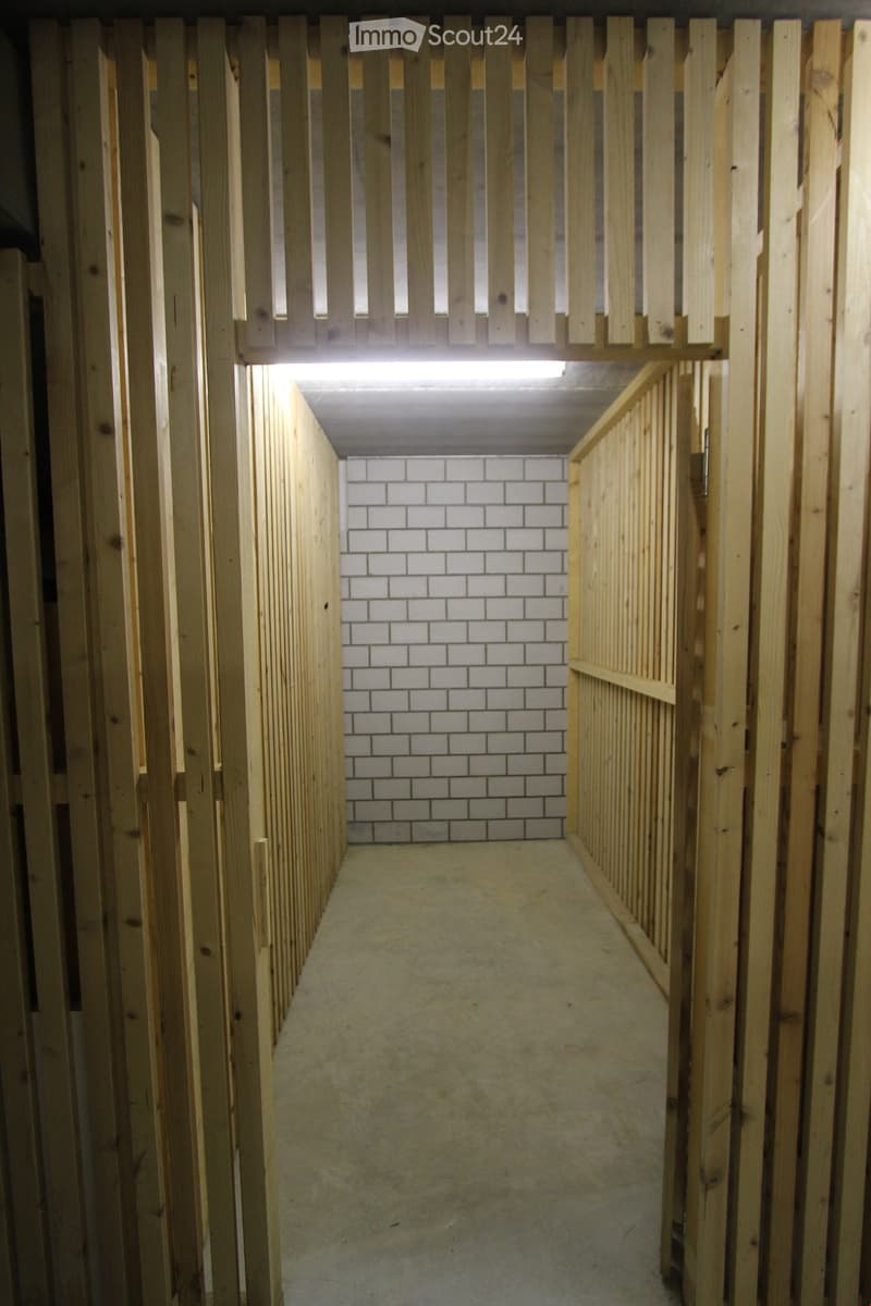 Empty wooden-framed corridor with white tiled walls and a concrete floor, featuring a raised wooden platform at the end.