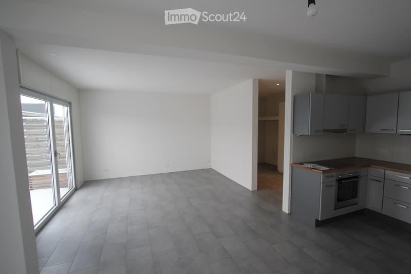 Empty kitchen with grey cabinets, wooden countertops, and tiled flooring. A large sliding glass door leads to an outdoor area.