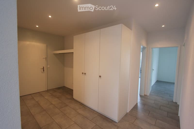 Empty hallway with tiled floor, white walls, built-in closet, and recessed lighting. Two doors lead to other rooms.