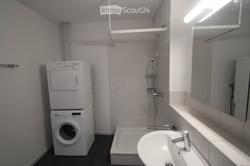 Bathroom with a bathtub, sink, mirror, and stacked washing machine and dryer.