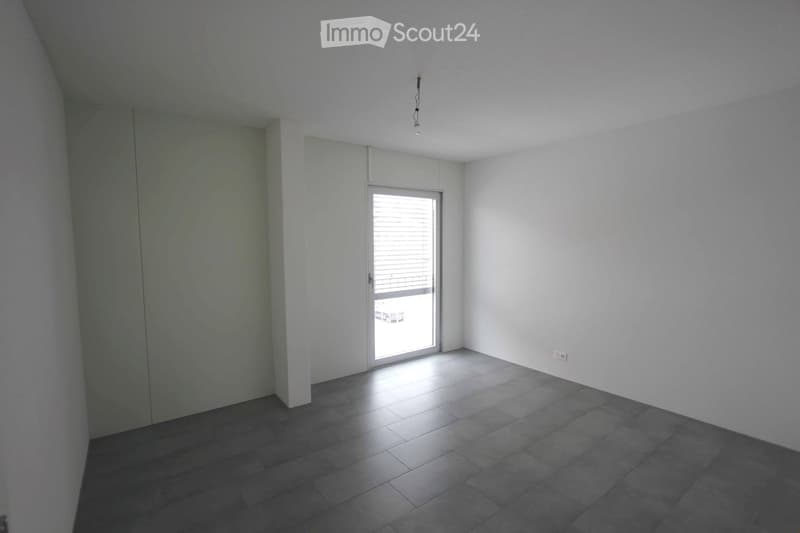Empty room with white walls, dark tiled floor, and a single window with blinds. No furniture or equipment present.