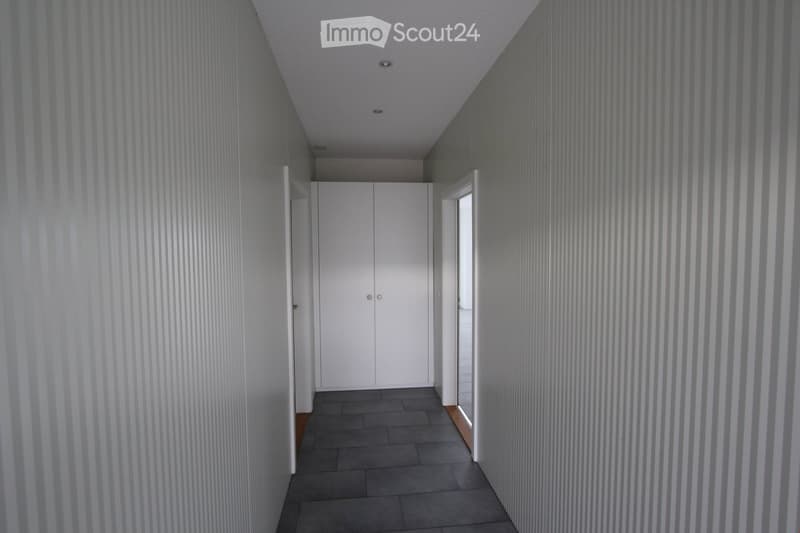 Modern hallway with grey tiled floor, white walls with vertical stripes, white double doors, and recessed ceiling lighting.