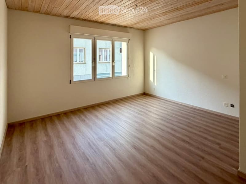 Empty room with wooden flooring, white walls, and large windows with blinds. No furniture or equipment present.