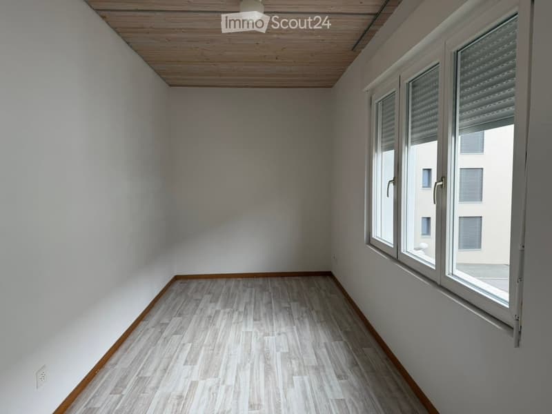 Empty room with white walls, wooden flooring, and large windows with blinds. No furniture or equipment present.