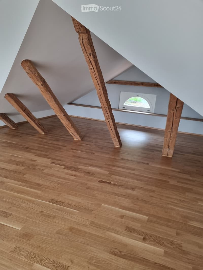 empty attic room with wooden beams, hardwood floor, and small window