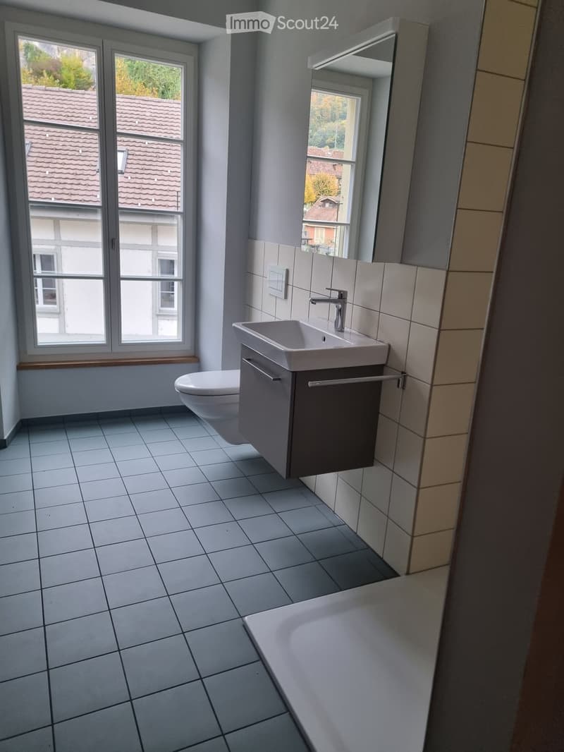Bathroom with toilet, white sink with faucet, mirror, tiled floor, window