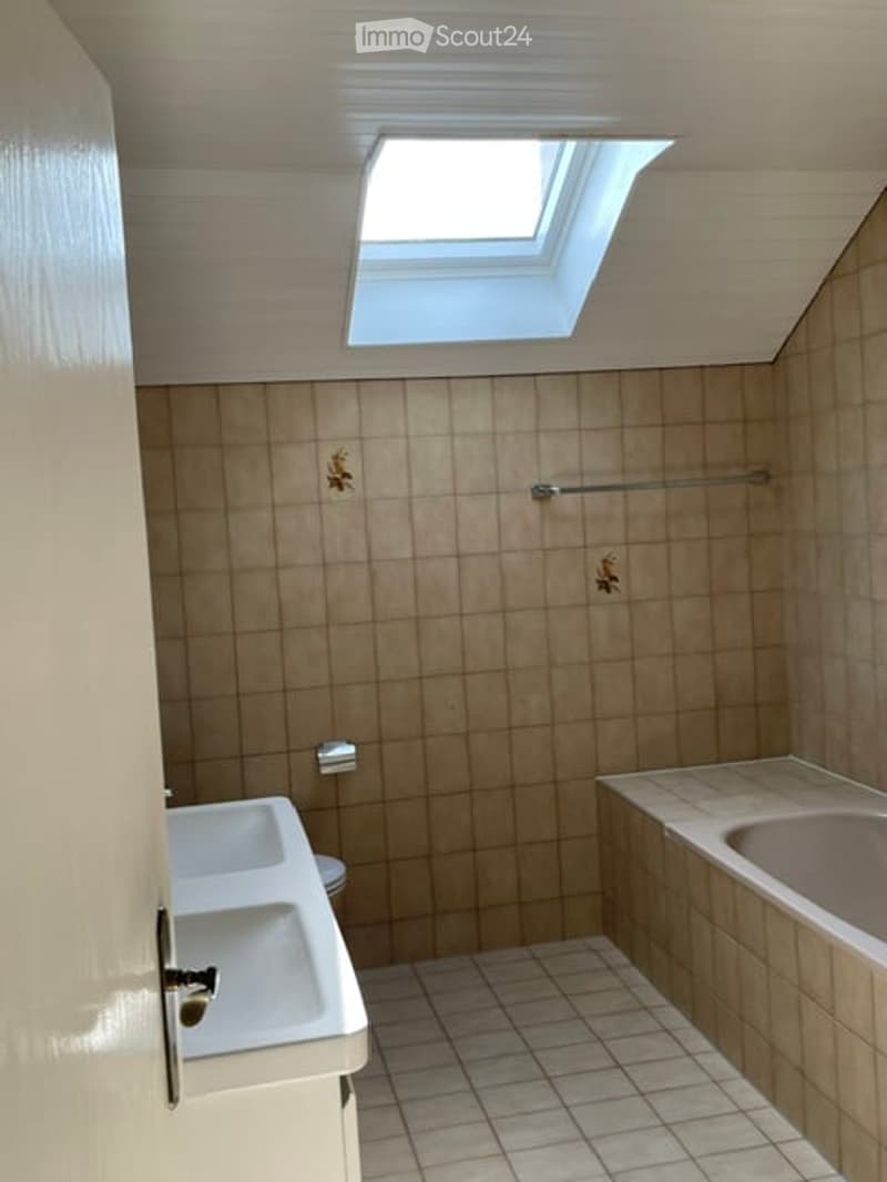 Bathroom with beige tiles, a window, a sink, a toilet, and a bathtub.